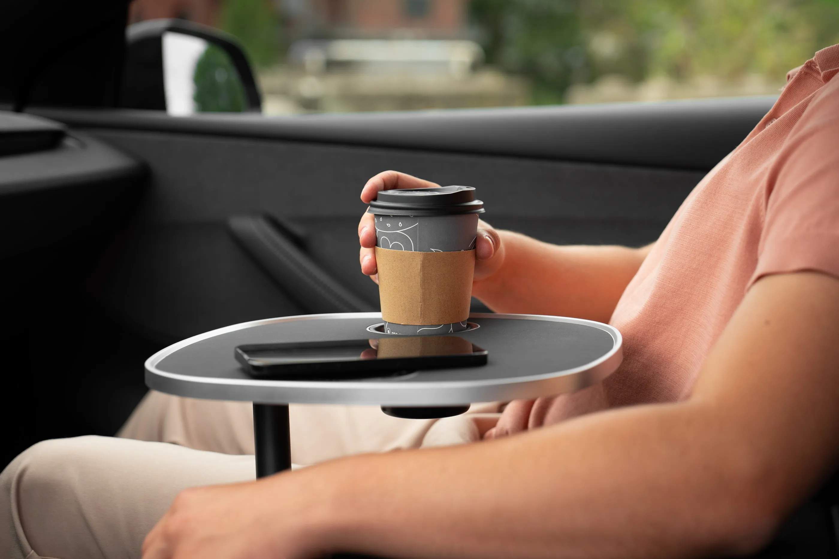 Kaffeebecher in der Getränkeaussparung der schwarzen Tischplatte, daneben ein flach liegendes Smartphone
