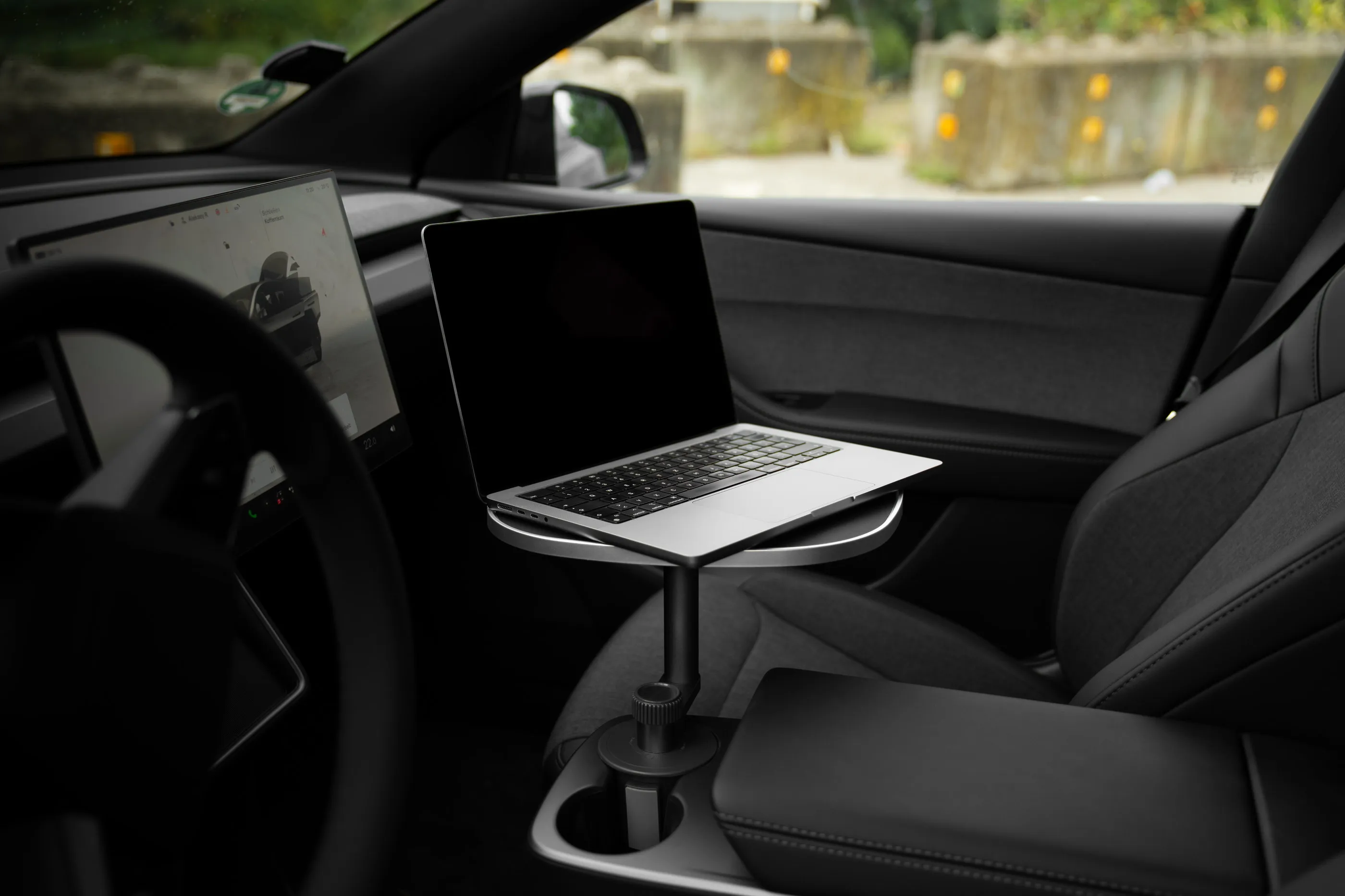Aufgeklappter Laptop auf der schwarzen Tischplatte über der vorderen Mittelkonsole eines geparkten Tesla