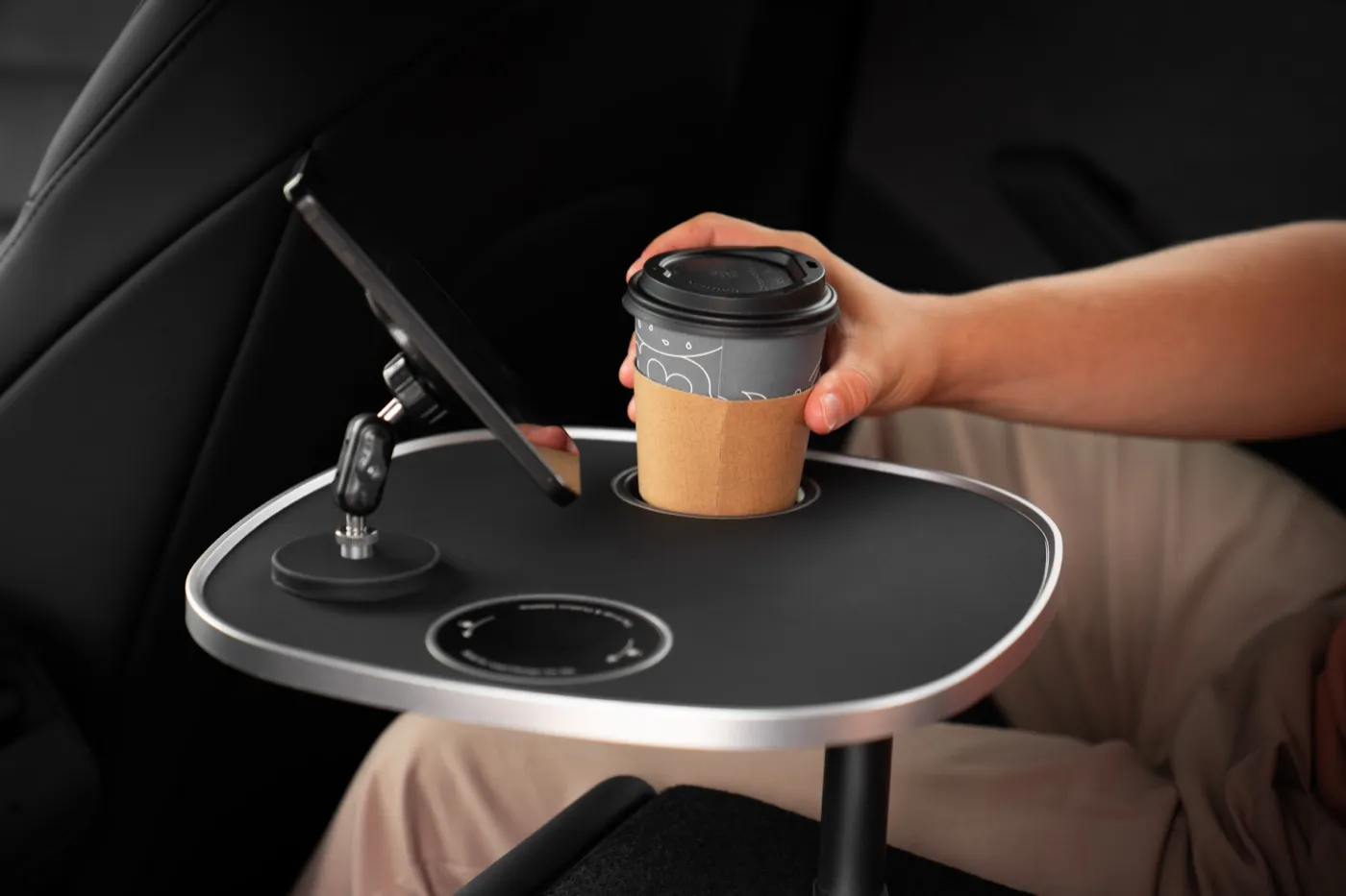 Magnetischer Handyhalter mit Smartphone auf der schwarzen Tischplatte über der Rückbank, daneben ein Kaffeebecher