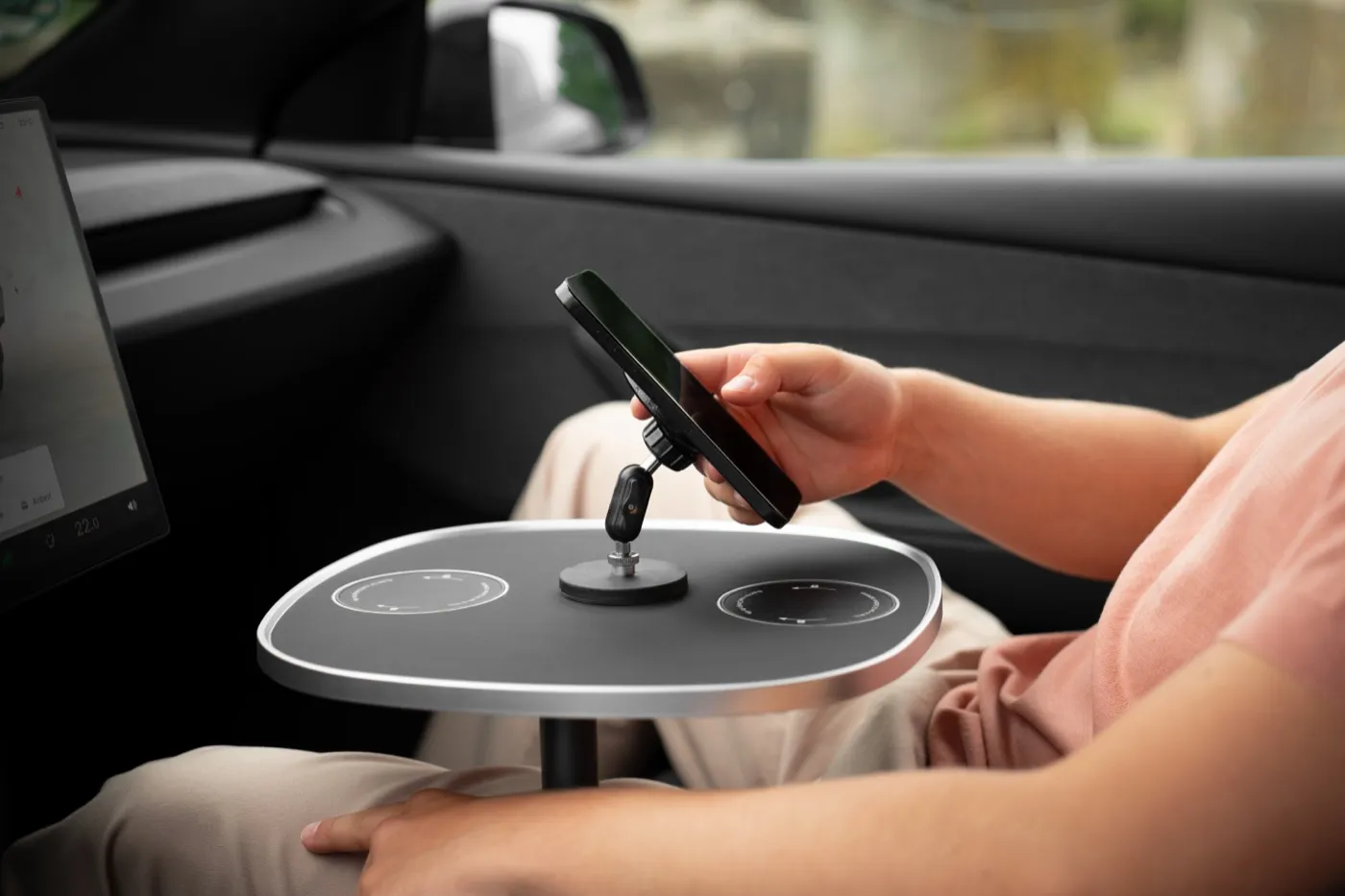 Hand am Smartphone, das magnetisch auf der schwarzen Tischplatte hält, links das Display des Fahrzeugs