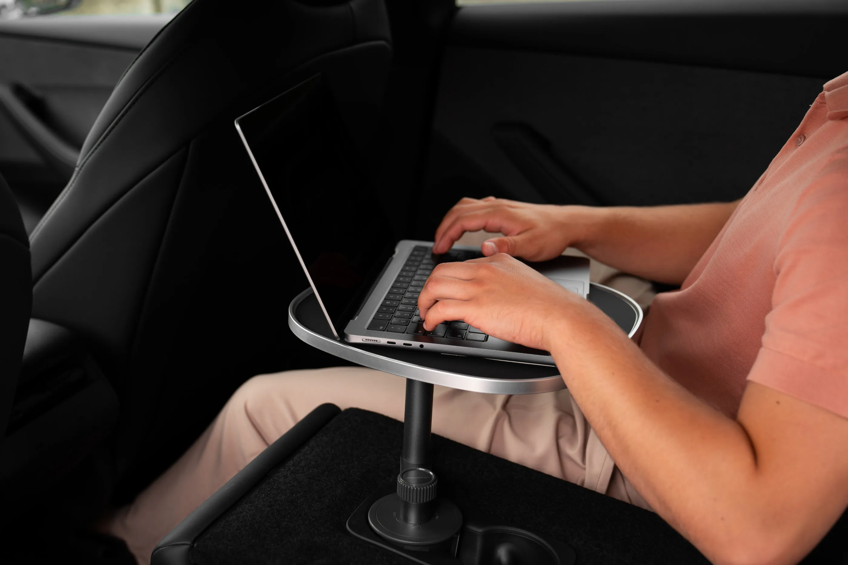 Person tippt an einem Laptop auf der schwarzen Tischplatte an der hinteren Mittelkonsole eines geparkten Tesla