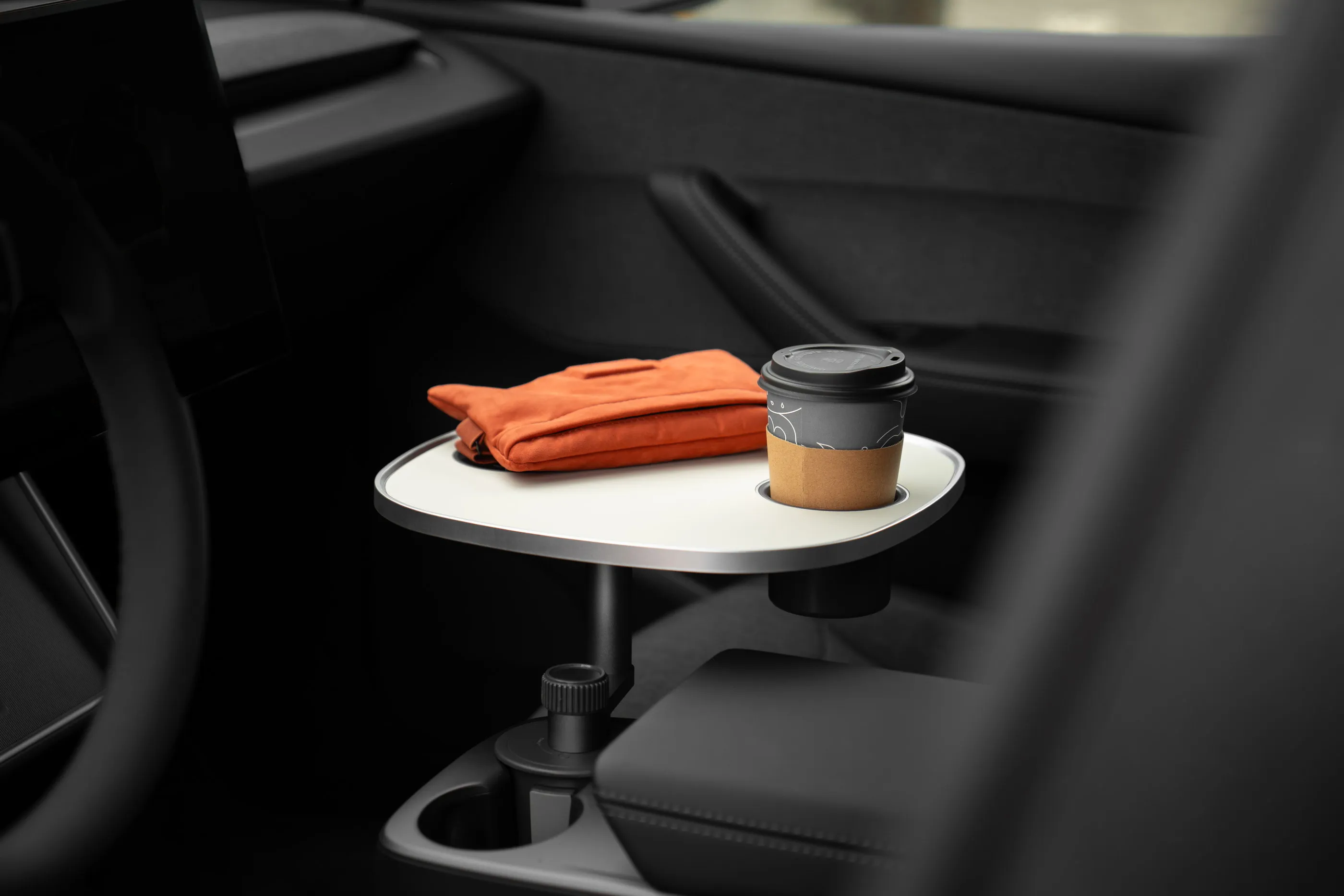 Kaffeebecher in der Getränkeaussparung der weißen Tischplatte, daneben ein zusammengelegtes Kleidungsstück