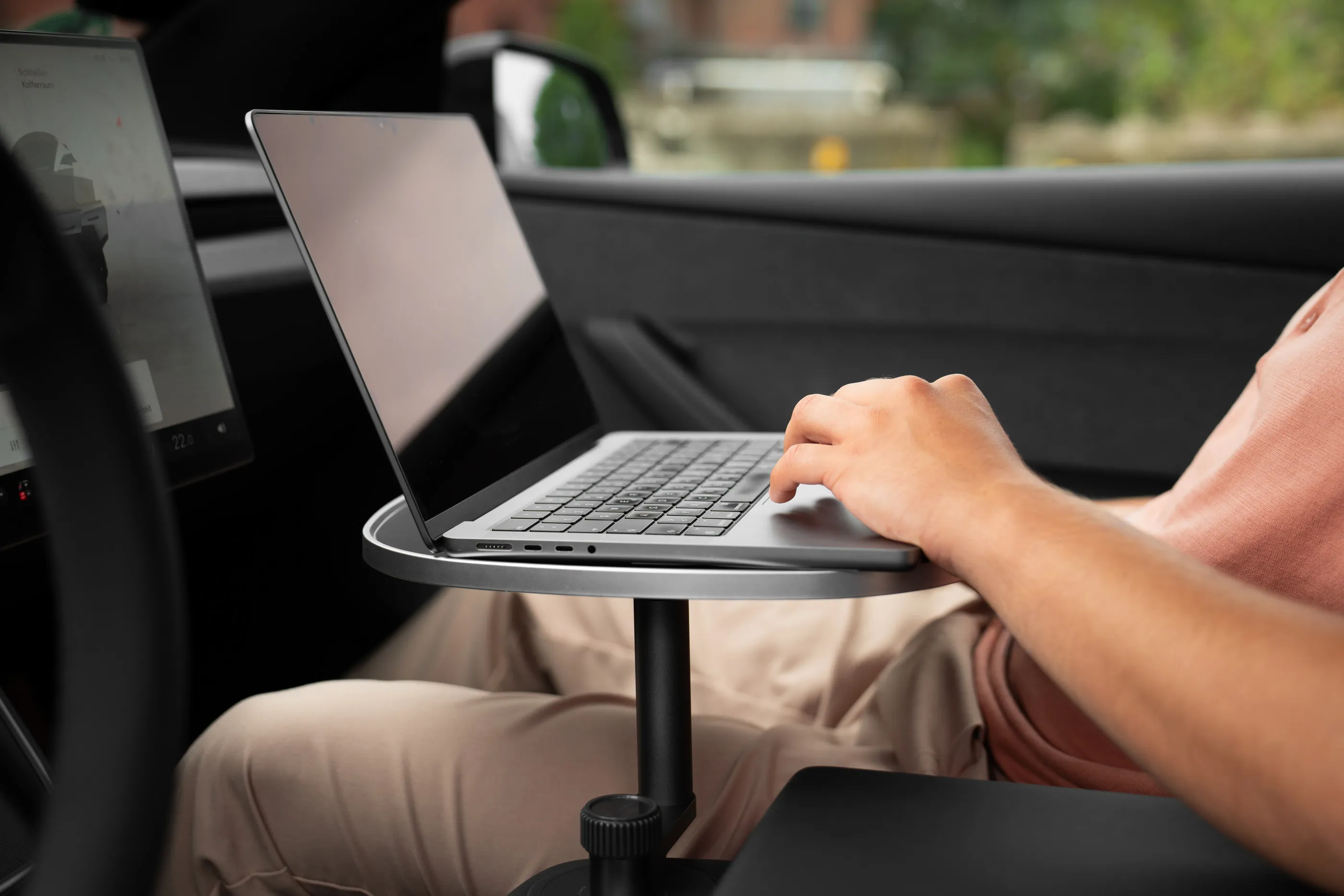 Person auf dem Beifahrersitz tippt an einem Laptop, der auf der weißen Tischplatte steht