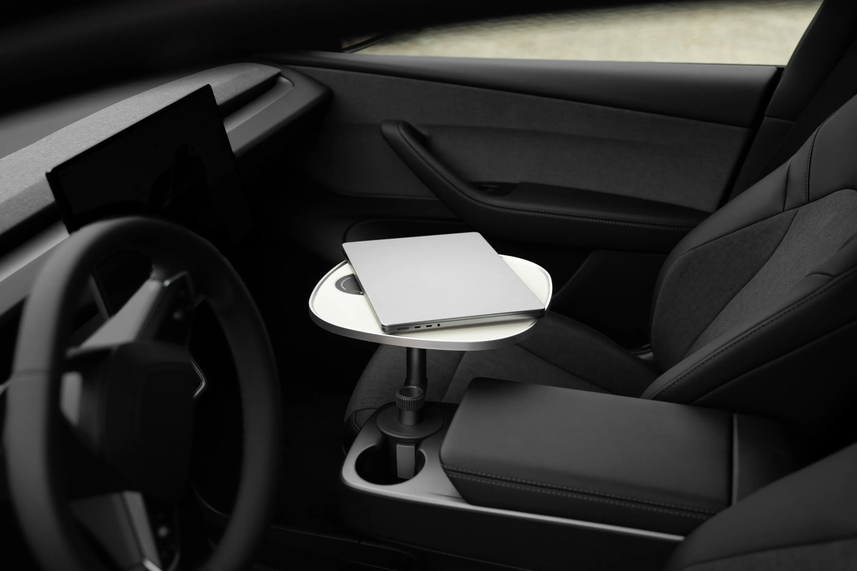 Zugeklappter Laptop auf der weißen Tischplatte über der Mittelkonsole eines geparkten Tesla