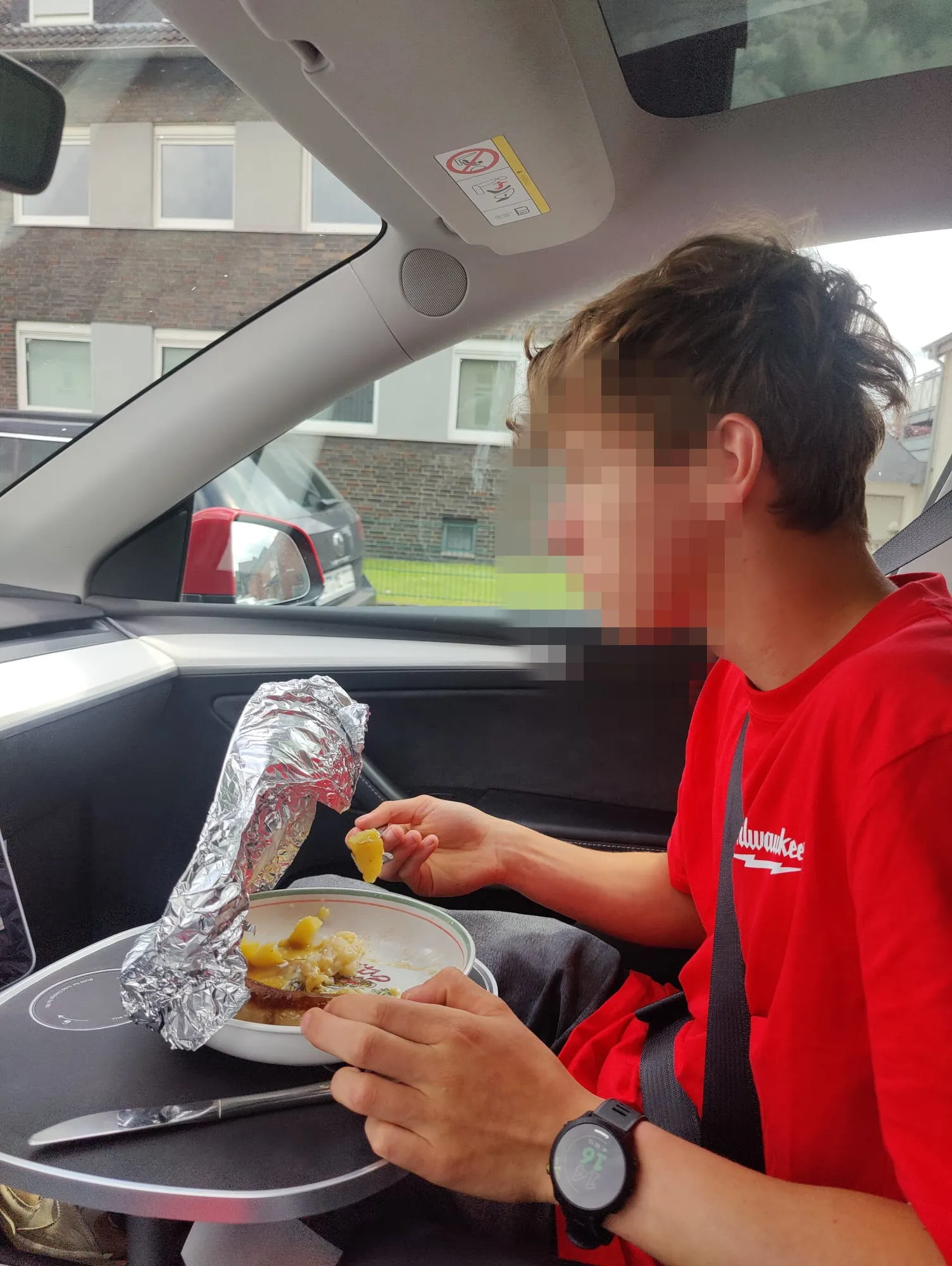 Kundenfoto: Teller mit Essen auf der Tischplatte auf der Beifahrerseite eines geparkten Tesla Model Y